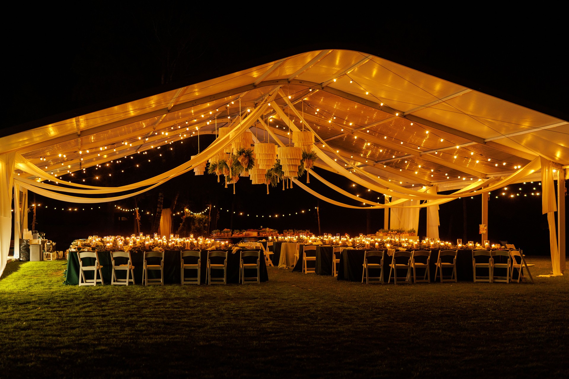 A large white event tent, decorated with twinkling string lights and a stunning chandelier, provides a romantic and enchanting atmosphere